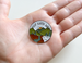 Camping Pin with Green Mountains, Trees, River, and Sky Scene with Saying "Keep Earth Wild"