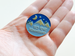 Camping Pin with Mountains, Pine Trees, Moon, and Blue Night Sky Scene with Saying "To The Mountains"