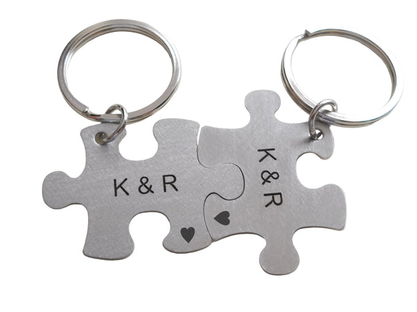 Two silver puzzle piece keychains with 'K&R' initials on a light gray background
