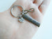 A close-up of a hand holding a metal keychain with a round key ring, a rectangular engraved bar, and a small heart charm that reads 'I love you'.