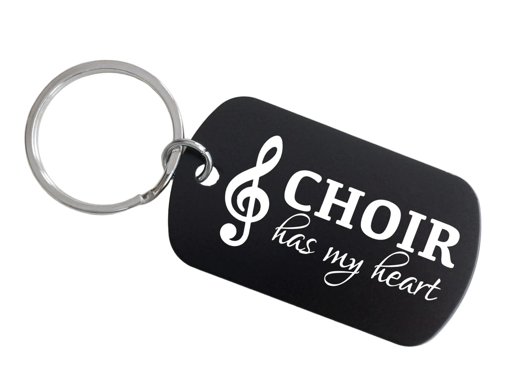 A black dog-tag style keychain with a silver metal key ring, featuring the white text 'CHOIR has my heart' and a white treble clef symbol, shown on a plain light background.