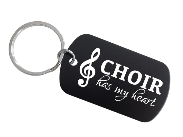 A black dog-tag style keychain with a silver metal key ring, featuring the white text 'CHOIR has my heart' and a white treble clef symbol, shown on a plain light background.