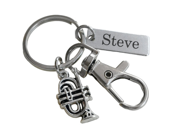 A silver-toned metal keychain with a split ring, a small trumpet charm, a lobster clasp, and a rectangular tag engraved with the name 'Steve', shown on a plain light background.